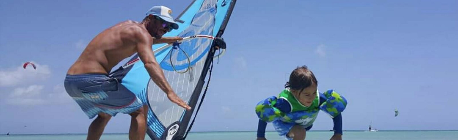 An instructor teaching a young child to windsurf in shallow water